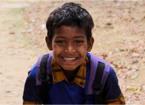 A smiling Santal schoolboy wearing a backpack outdoors