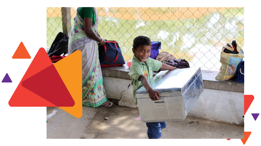 A smiling Santal boy carrying a metal storage trunk