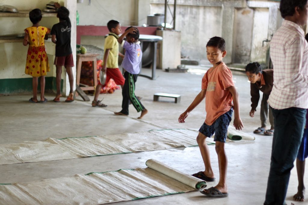 A boy playing on rolled mats with other children in the dining hall