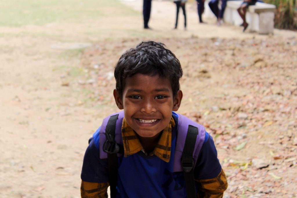 A smiling Santal schoolboy wearing a backpack
