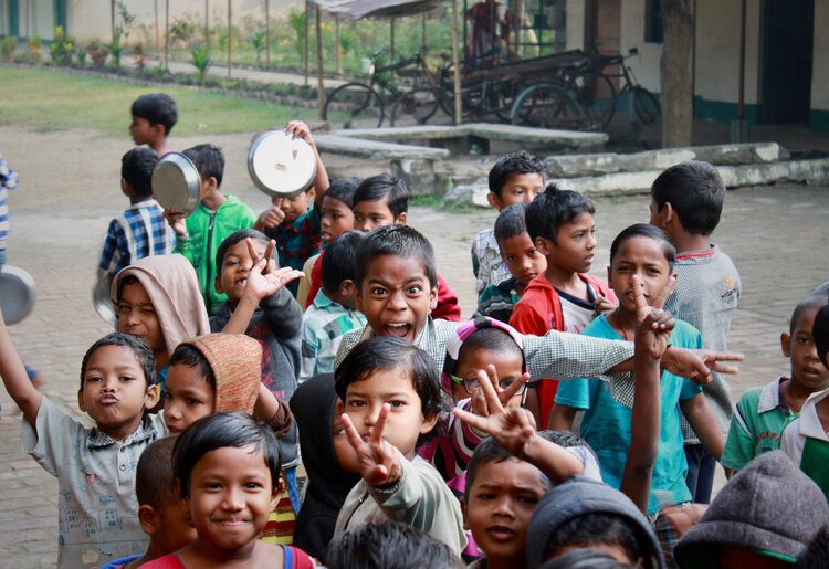 Village children in Gurap, India smiling and waving, some making peace signs