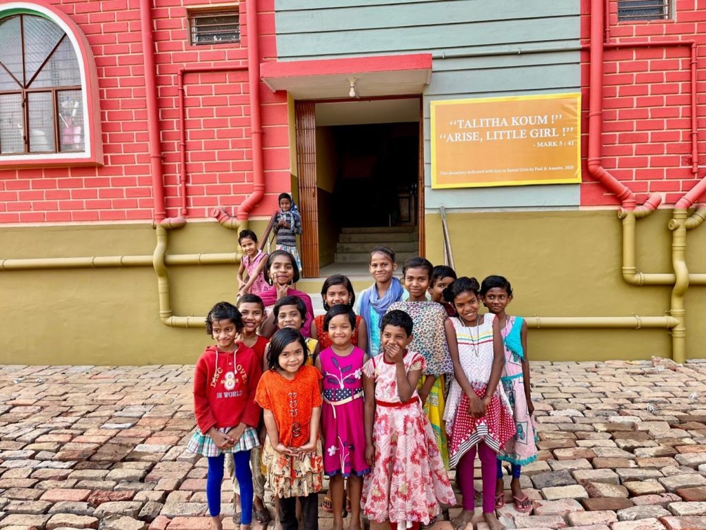 Santal girls in front of the girls' dormitory with a banner reading Talitha Koum, Arise Little Girl
