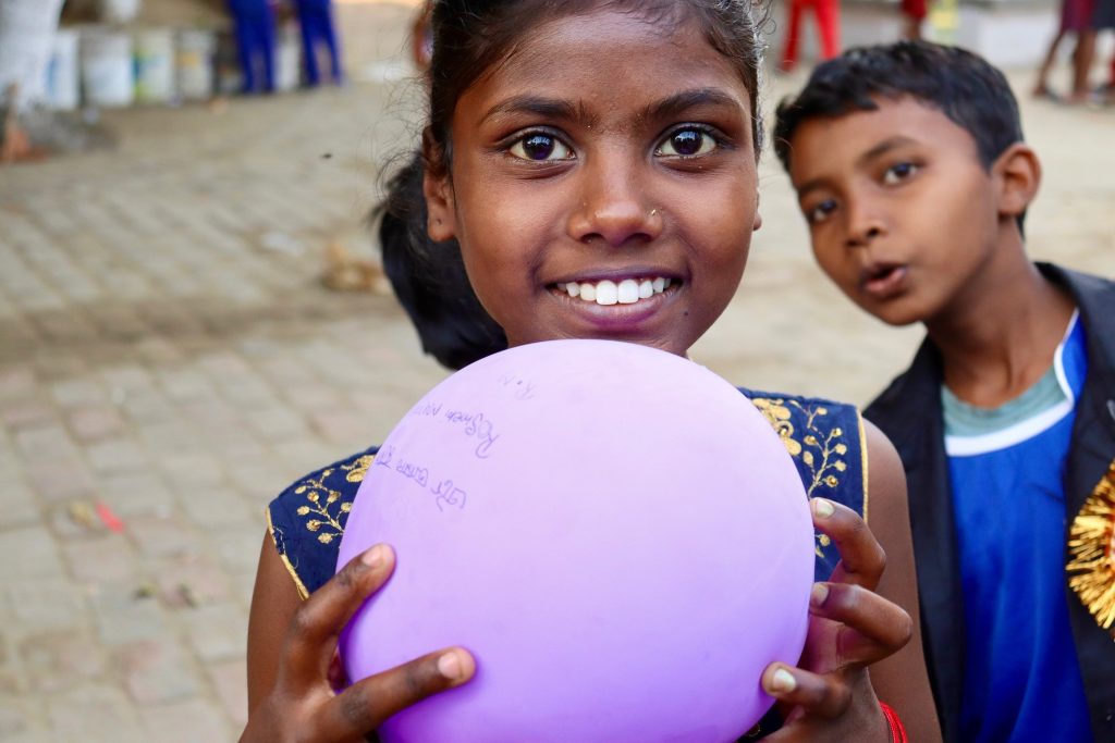 A smiling Santal girl holding a ball with a friend beside her